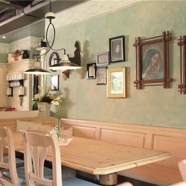 Ein gemütlicher Raum mit Holzstühlen und einem langen Tisch. An der Wand hängen verschiedene Bilder und Fotografien.