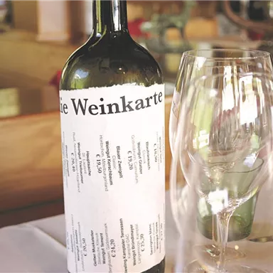 Eine Flasche Wein steht neben einem Glas auf einem Tisch. Die Etikette der Flasche zeigt die Weinkarte an.