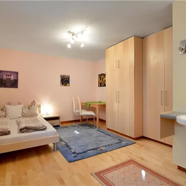 A cozy bedroom with a double bed, a desk, and a large wardrobe. The walls are painted in soft colors and there is a carpet on the floor.