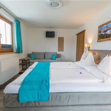 Ein modernes Hotelzimmer mit einem Doppelbett und einem gemütlichen Sitzbereich. Große Fenster sorgen für viel natürliches Licht und eine angenehme Atmosphäre.