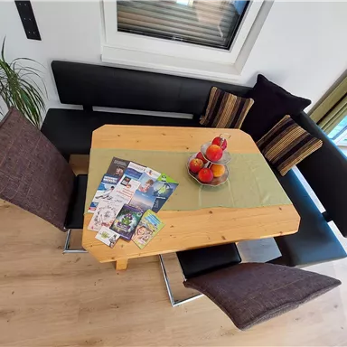 Ein gemütlicher Essbereich mit einem Holztisch und bequemen Sitzen. Auf dem Tisch liegen einige Magazine und eine dekorative Schale mit Äpfeln.