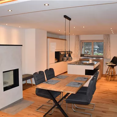 Eine moderne Küche mit einem Essbereich und einem Kamin. Der Raum ist hell und einladend, mit Holzfußboden und eleganten Möbeln.