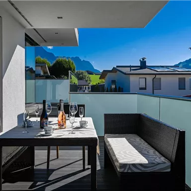 Ein schöner Balkon mit Blick auf Berge und eine klare blaue Himmel. Der Tisch ist gedeckt mit Glaswaren und einer Flasche Wein.