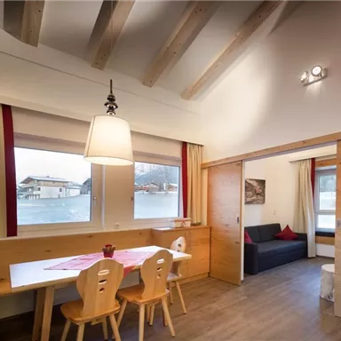 A cozy living kitchen with a table and chairs. The room has large windows with a view of the surroundings and is designed to be bright and friendly.