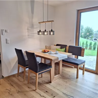 Ein modernes Esszimmer mit einem Holztisch und Stühlen. Große Fenstertüren bieten einen Blick auf den Garten.