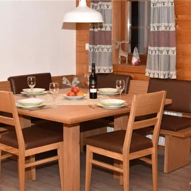 A cozy dining area with a wooden table and chairs. The table is nicely set, and there is a bottle of wine as well as fruit in the center.