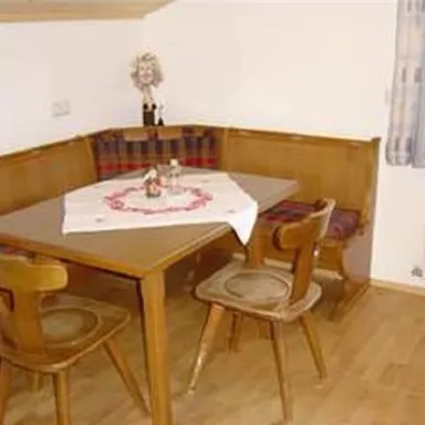 A cozy dining area with a wooden table and chairs. The walls are simple and the windows let in plenty of light.