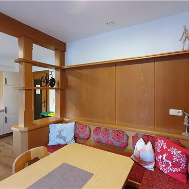 Ein gemütlicher Essbereich mit Holzverkleidung und bunten Kissen. Die offene Küche ist im Hintergrund sichtbar.