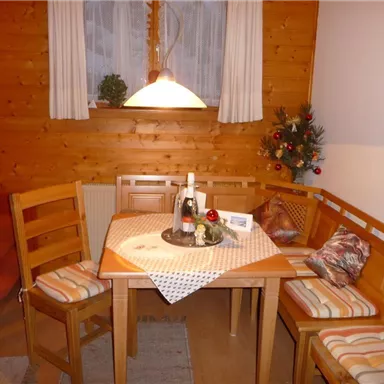 A cozy dining area with a table and wooden chairs. On the table are a bottle of sparkling wine and festive decorations.