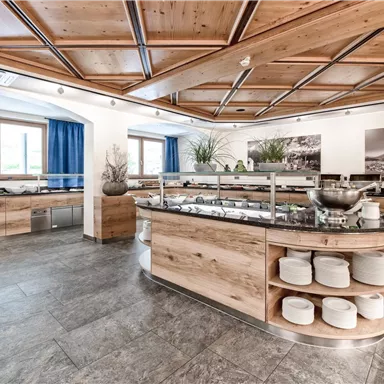 A modern kitchen with wooden shelves and a large buffet. Bright windows create a friendly atmosphere.