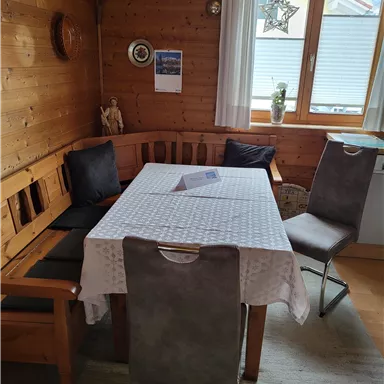 A cozy dining area with wooden walls and a table covered with a white tablecloth. Two chairs and a bench are placed around the table.