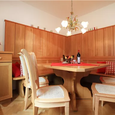 Ein gemütlicher Essbereich mit Holzverkleidung und einem rustikalen Tisch. Auf dem Tisch stehen Wein und Obst, ergänzt durch bequeme Stühle.