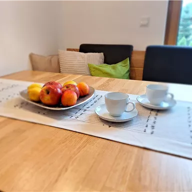 Ein Tisch mit einer Schalen voller Äpfel und zwei Tassen. Die Atmosphäre ist gemütlich mit einem hellen Holzdesign und dekorativen Kissen.