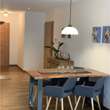A modern dining area with a wooden dining table and blue chairs. Two pictures are hung on the wall, and the lighting creates a cozy atmosphere.