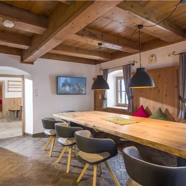 A modern dining area with a long wooden table and stylish chairs. The walls are rustic with wooden elements and there are large windows with a view outside.