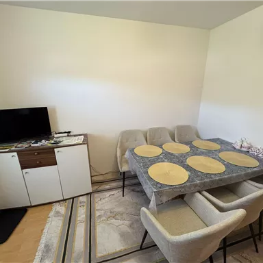 Ein moderner Essbereich mit einem eleganten Tisch und Stühlen. Im Hintergrund steht ein Fernseher und ein Sideboard.