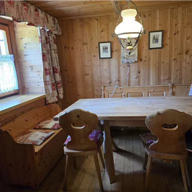 Ein gemütlicher Raum mit Holzwänden und einem großen Tisch. Die Einrichtung umfasst eine Bank und eine Deckenlampe für eine warme Atmosphäre.