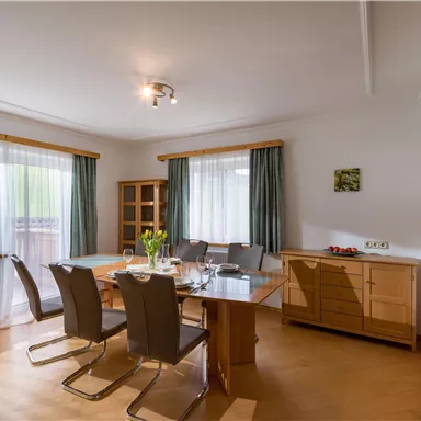 A bright dining room with a large table and modern chairs. Large windows provide plenty of daylight and a cozy atmosphere.