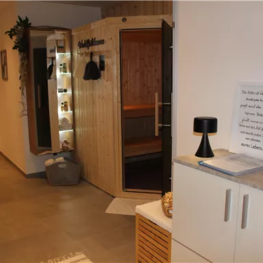 Ein gemütlicher Empfangsbereich mit einer Holzsauna. Auf der linken Seite stehen Pflanzen und ein Tisch mit Dekoration.