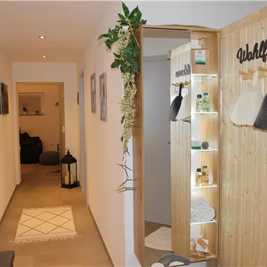 Ein einladender Flur mit natürlichen Holzelementen und einem Bereich für Wohlfühlprodukte. Gemütliche Dekoration und sanftes Licht schaffen eine entspannende Atmosphäre.