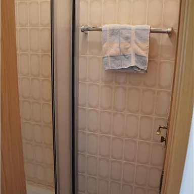 Ein kleines Badezimmer mit einer Dusche und einem Handtuch. Die Wände sind in einem hellen, gemusterten Design gehalten.