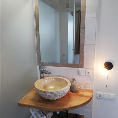 A modern bathroom with a stylish stone sink. The wooden shelf provides space for towels and toiletries.