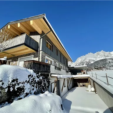 A modern house in the snow with a clear blue sky. Majestic mountains are visible in the background.