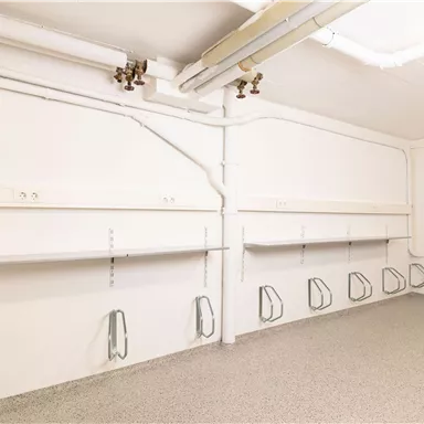 An empty room with white walls and a gray floor. There are shelves and brackets on the walls.