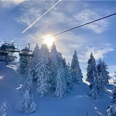 A picturesque winter landscape with snow-covered trees and a ski lift. The sun shines over the snow-rich hills.