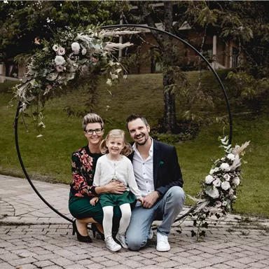 A family poses happily in front of a decorative flower arch. They sit together and radiate joy.