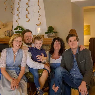 Eine Gruppe von fünf Personen posiert in einem gemütlichen Innenraum. Sie lächeln freundlich und tragen traditionelle Kleidung.