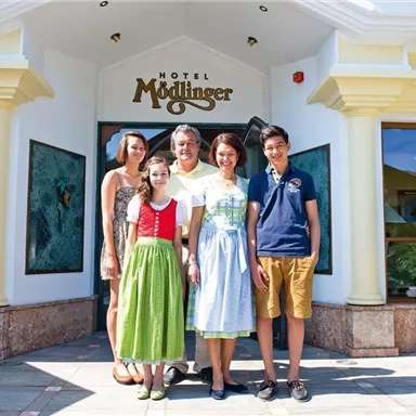 A family stands in front of the Hotel Mödlinger. They are smiling and wearing traditional clothing.