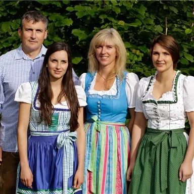 A group of four people wearing traditional Bavarian costumes. They are smiling in front of a green backdrop.