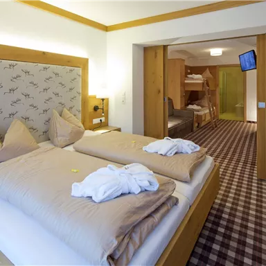 A cozy room with a double bed and two bedspreads. In the background, there is another bed as well as a television.