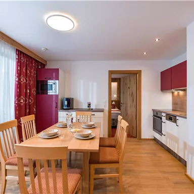 Eine moderne Küche mit einem Esstisch und Stühlen. Die Wände sind hell, und es gibt große Fenster mit Vorhängen.