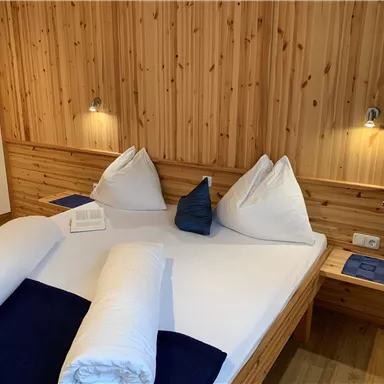 Ein gemütliches Schlafzimmer mit Holzverkleidung und einem großen Doppelbett. Es gibt gemütliche Kissen und dekorative Elemente auf den Nachttischen.