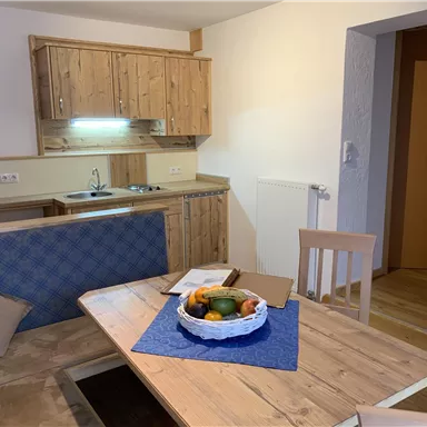 Eine gemütliche Küchenzeile mit Holzregalen und einem Esstisch. Auf dem Tisch liegt eine Fruchtschale und ein blauer Tischläufer.