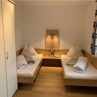 Ein gemütliches Zimmer mit zwei Einzelbetten und Holzmöbeln. Es gibt einen Kleiderschrank und eine angenehme Beleuchtung.