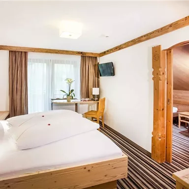 A spacious hotel room with wooden furniture and two beds. The room features a window overlooking a small table and television.