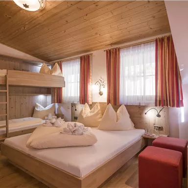 Ein gemütliches Zimmer mit Holzdekor und hellen Vorhängen. Es gibt ein Doppelbett, ein Hochbett und eine gemütliche Sitzecke.