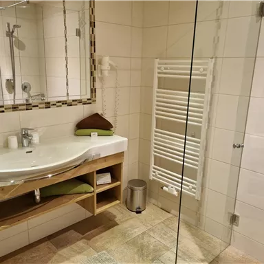 A modern bathroom with an elegant sink unit and mirrored cabinets. The shower is separated by a glass wall, and a towel radiator is also available.