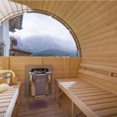 Ein gemütlicher Wellnessbereich mit Holzverkleidung und Blick auf die Berge. Handtücher und ein Eimer sorgen für eine entspannte Atmosphäre.