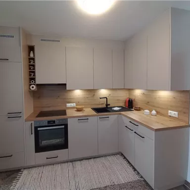 Eine moderne Küche mit hellen Möbeln und Holzdetails. Die Ausstattung umfasst einen Herd, einen Ofen und eine elegante Spüle.