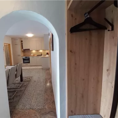 Ein schmaler Durchgang mit einem Kleiderständer und Blick auf eine moderne Küche. Der Boden ist mit Fliesen und Teppich ausgestattet, was eine einladende Atmosphäre schafft.