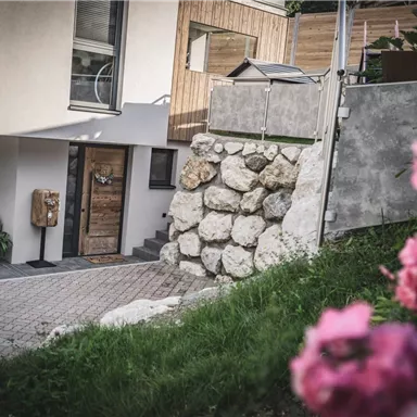 A modern house with a stone wall and a beautiful entrance. In the foreground, pink flowers are blooming.