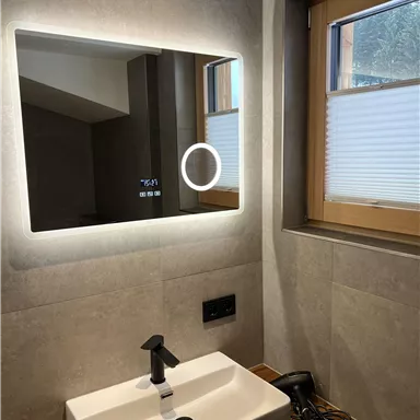 Ein modernes Badezimmer mit einem beleuchteten Spiegel und einem weißen Waschbecken. Durch das Fenster scheint natürliches Licht herein.