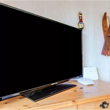 A black television stands on a wooden table in a cozy room. In the background, decorative skis and a checked wall are visible.