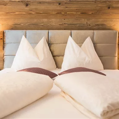 Ein gemütliches Schlafzimmer mit einem großen Bett und zwei Kopfkissen in Form von Spitzen. Sanfte Beleuchtung und Holzverkleidung verleihen eine einladende Atmosphäre.