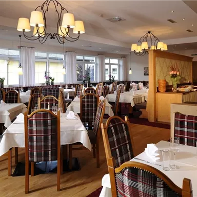 Ein elegantes Restaurant mit gedeckten Tischen und Holzmöbeln. Große Fenster sorgen für viel Tageslicht und einen gemütlichen Eindruck.