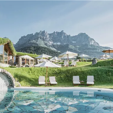 A beautiful outdoor area with a pool and loungers. In the background, majestic mountains rise under a clear sky.